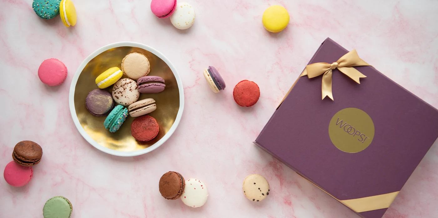 A bowl and a gift box filled with colorful Woops! macarons